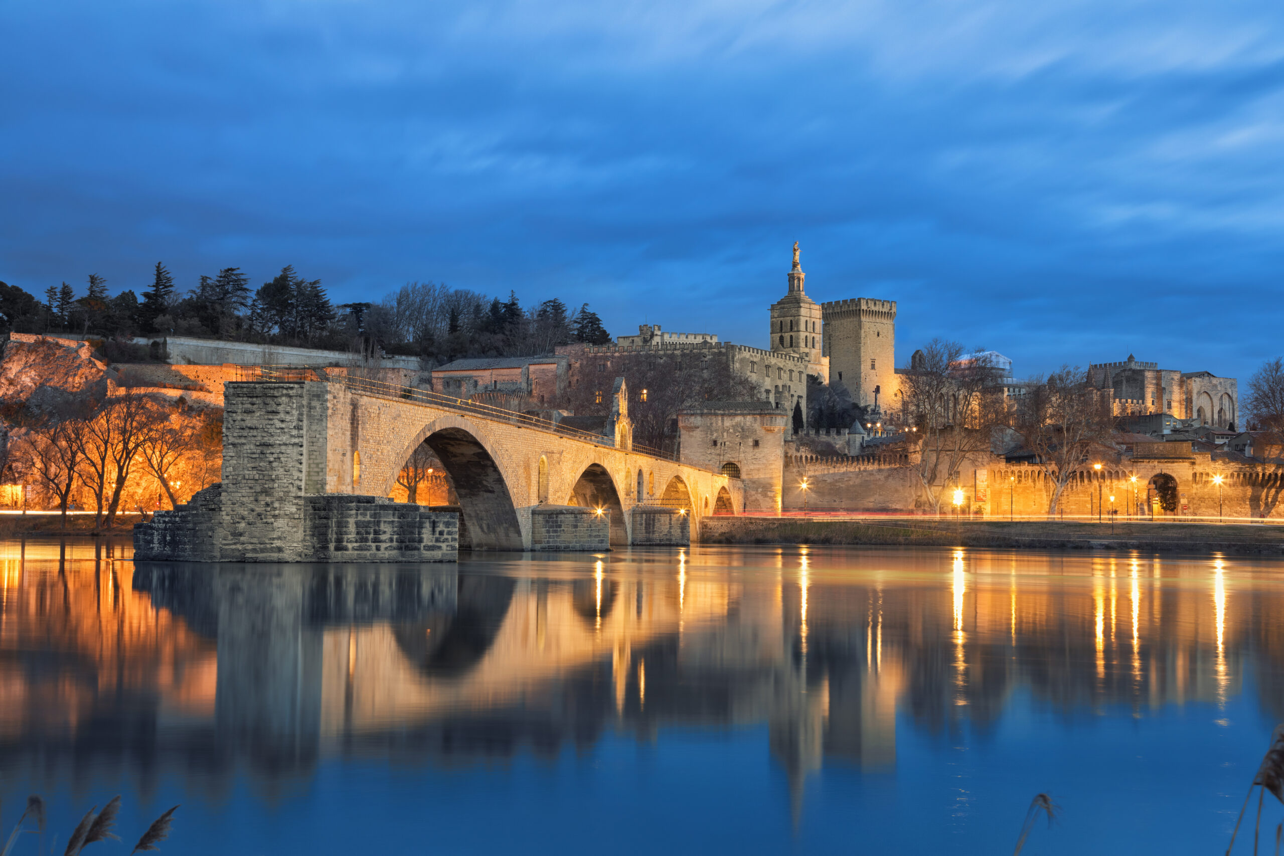 View on Pont d'Avignon 12th century bridge and city skyline reflecting in water at dusk in Avignon, Provence, France