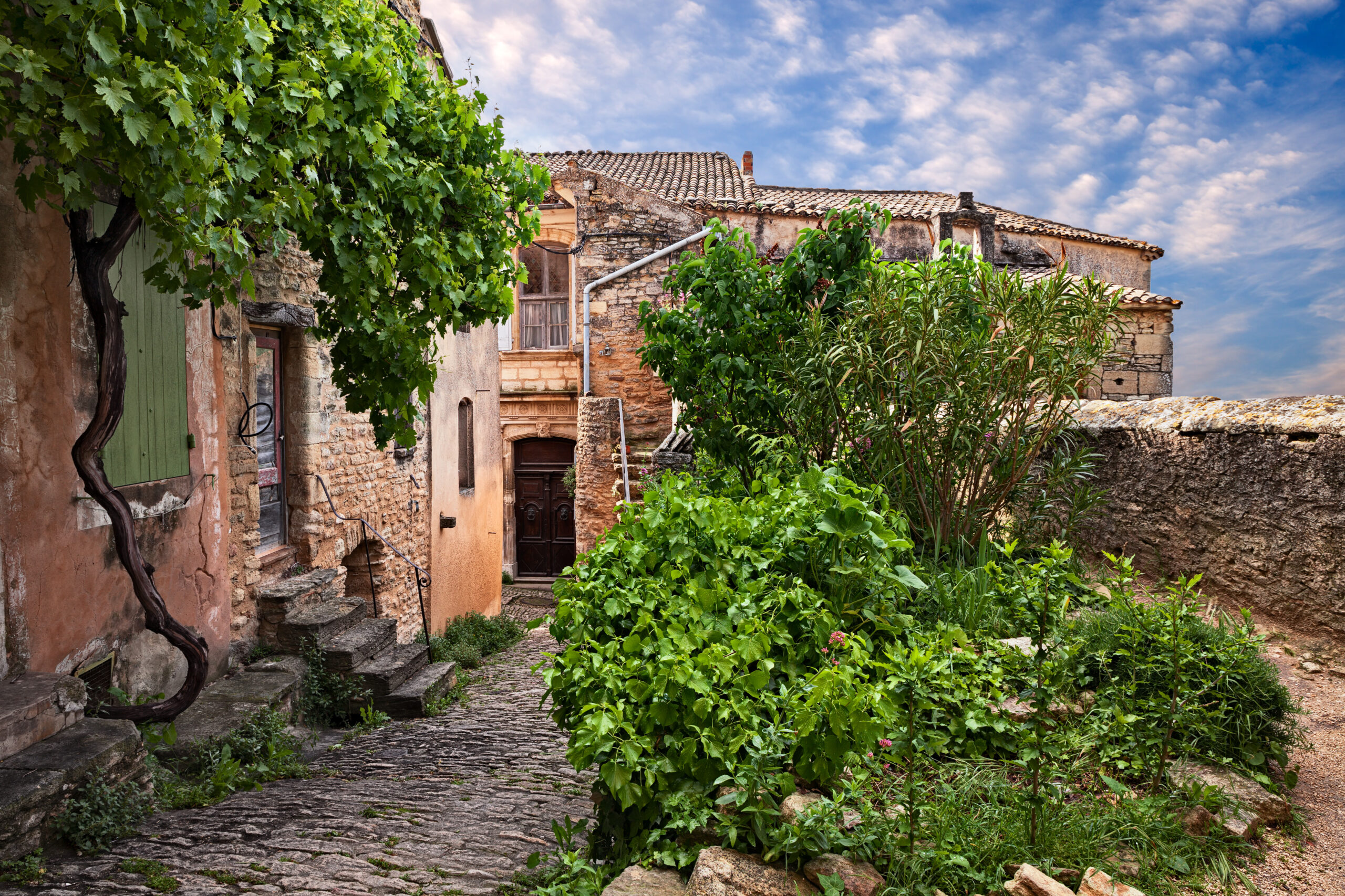 Gordes, Vaucluse, Provence, France: picturesque corner in the old town with a narrow alley, old houses and a grapevine pergola